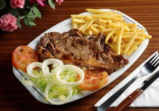 Plato combinado de chuleta de ternera con patatas fritas y ensalada.