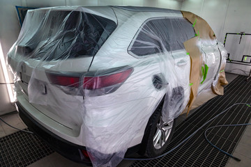 The white SUV in the garage box is covered with a protective film and the details are sealed with professional paper and the front right door of the car is painted with a paint-and-lacquer solution.