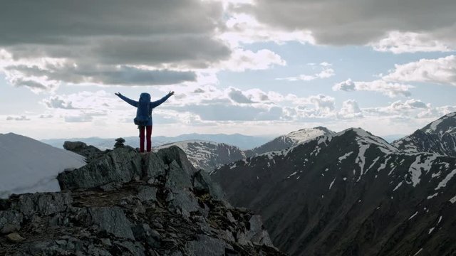 successful young woman backpacker open arms on mountain peak