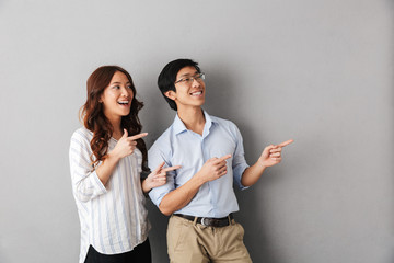 Cheerful asian couple standing isolated over gray