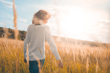 Girl in a white sweater and jeans in a field with spikelets against the blue sky in the rays of the sun