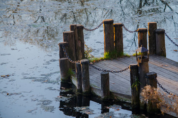 The old bridge is a bridge on a river of logs connected by chains. In the river, the reflection of trees.