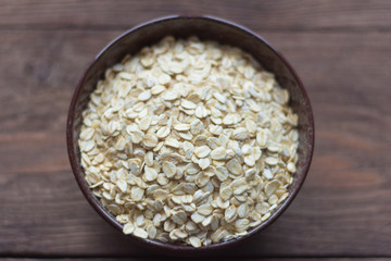 oat flakes, oat in dark bowl on wooden background