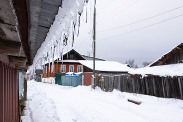 Fototapeta premium icicles on the roof of a rural house, rural winter landscape