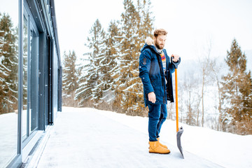 Portrait of a man in winter clothes standing with snow shovel on the terrace of the building in the...
