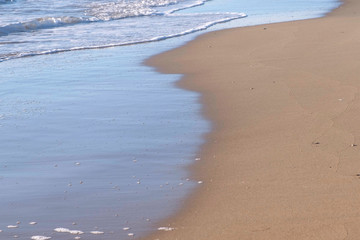 Long sea waves with foam on the sandy beach.