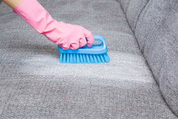 Dry cleaner's employee hand in protective gloves removing stain from gray sofa with brush and...