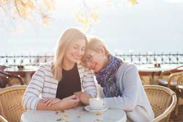 Mother and her adult daughter are hugging. Beautiful women in autumn street cafe outside. Happy...