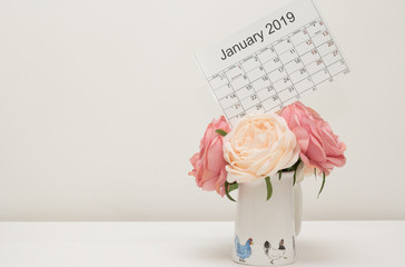 Close-up: calendar of January 2019 with festive dates is on top a bouquet of pink and beige flowers on white background. Concept: Happy New Year & winter holidays. 
