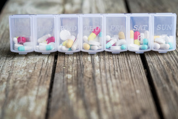 Variety of pills in white plastic pill organizer on weathered wood