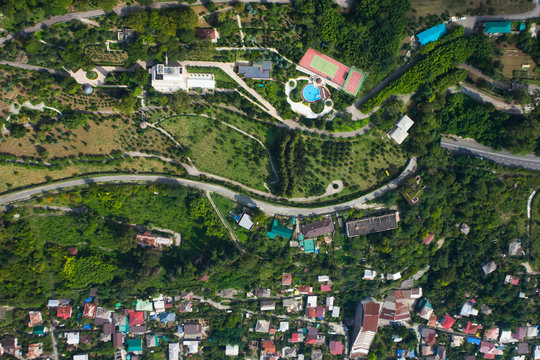 Hotel in a green forest, view from the top down. The road goes around the buildings, a bright blue pool is visible.