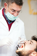 Obraz na płótnie Canvas Serious mature male dentist holding a syringe and giving anesthetics to worried young male patient. Health care and medicine concept