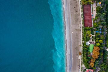 Hotels among the green park on the seafront with turquoise water and the beach. top down