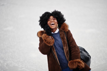 Curly hair african american woman wear on sheepskin coat and gloves with backpack posed at winter day.