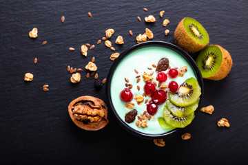 Healthy food colorful Yogurt Breakfast Bowl  with kiwi, flax seeds, Granola, and red currants in black ceramic bowl with copy space