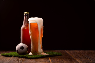 Photo of buttle and glass of beer, soccer ball on green grass