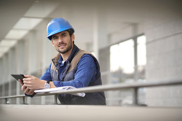 Handsome building expert in hardhat outdoors with tablet and blueprint