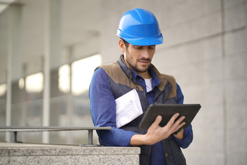 Handsome building expert in hardhat outdoors with tablet and blueprint