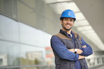 Smiling industrial worker in hardhat infront of modern building