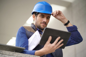 Handsome building expert in hardhat outdoors with tablet and blueprint