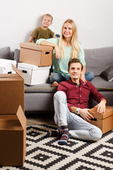 Image of parents with their son sitting on gray sofa with cardboard boxes