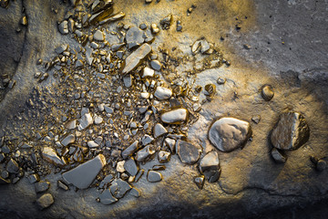 A pile of Gold nugget grains, on big river stone. Golden texture.