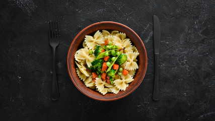 Farfalle pasta with vegetables on the plate. Top view. On a black background. Free copy space.