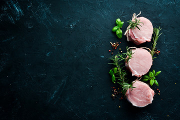 Raw meat, medallions with rosemary and spices. On a black stone background. Top view. Free copy...