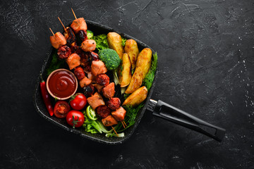 Chicken shish kebab with potatoes and vegetables on a black background. Meat. Top view. Free copy...