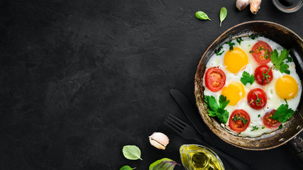 Eggs with tomatoes and greens in a frying pan.