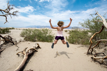 Young adult female woman jumps in the Mesquite Sand Dunes in Death Valley National Park in...