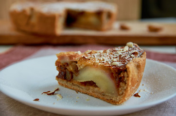 A piece of pear pie with nuts on the white plate. Sliced pear cake on the blurred background. Close up view