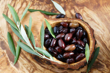 Fresh brown kalamata olives and olive tree leaves in authentic greek wooden bowl with bark, close up view