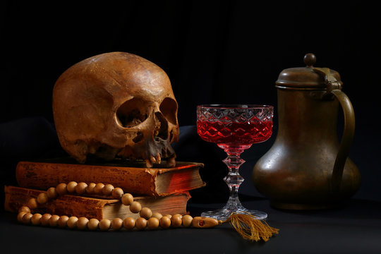 Skull, books, a glass of red wine and a bronze jug