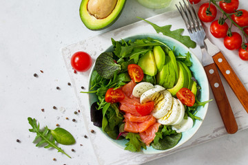 Diet menu, Vegan food. Healthy salad with arugula, Tomatoes, Salmon, Egg and Avocado on a white stone table. Top view flat lay background. Copy space.