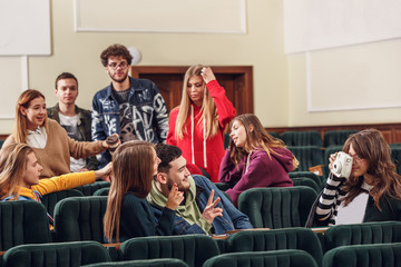 The group of cheerful students sitting in a lecture hall before lesson. The education, university, lecture, people, institute, college, studying, friendship and communication concept