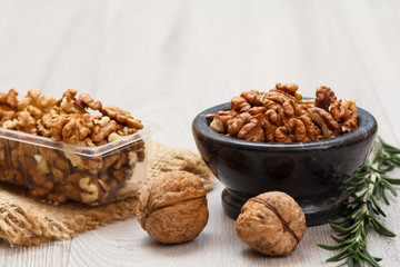 Walnuts in stone bowl and plastic container on a wooden background.