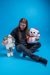 Fototapeta na wymiar Long-haired man looking down at Santa's toy while holding a snowman and sitting down. Funny gifts idea for Christmas holiday
