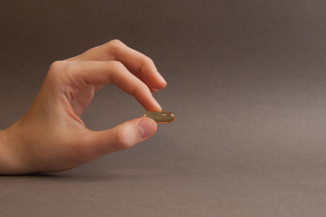 fish oil capsule in hand on grey background