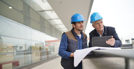 Workmen in hard hats consulting over blueprint on modern building sight