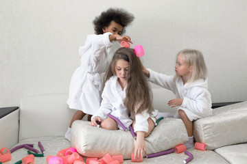 Little girls play with hair curlers and hairpins. Girls girlfriends in white coats braid curlers and hair clips each drg in her hair.