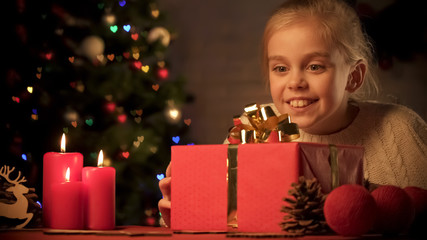 Little girl enjoying big Christmas giftbox on table with beautiful decorations