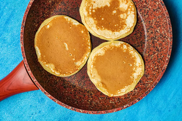 Ruddy pancake in a pan on a blue background. Close-up. View from above.