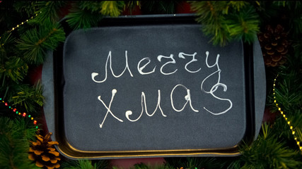 Merry Christmas phrase written with cream on baking tray, decorations for party