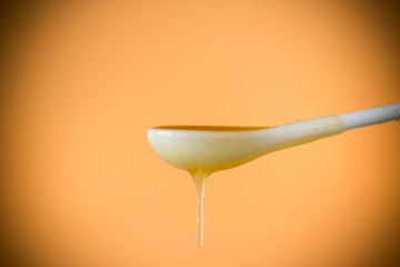 sweet honey flowing down from a spoon on an orange