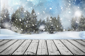 Empty wooden surface for product montage with falling snow and nice view of Christmas trees in winter time.