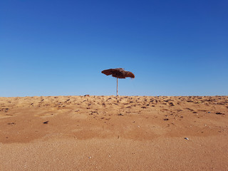 sun umbrella parasol on sand beach during hot summer sunny day against blue sky. low angle view background. - Powered by Adobe