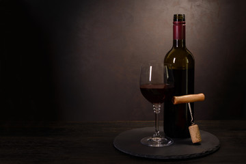 Fototapeta na wymiar Wine bottle, glass with red wine and cork with corkscrew on dark wooden background. Celebration concept. Copy space