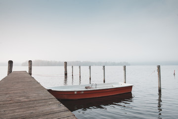 rotes Ruderboot welches an einem Holzsteg befestigt wurde. Aufgenommen an einem nebeligen Tag im Spätherbst.