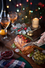 A hand is cutting a grilled pork loin on the Christmas table with Christmas lights in the background.